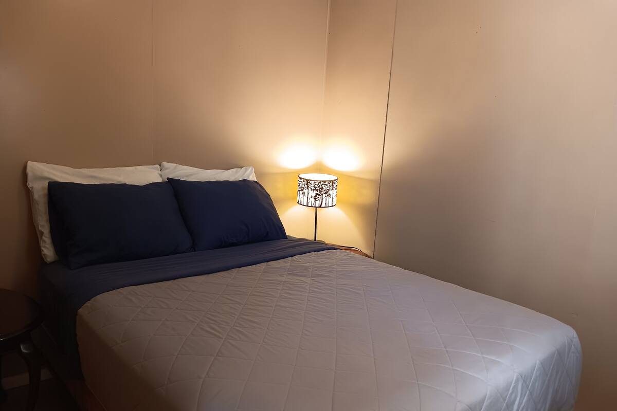 A neatly made bed with a quilted duvet and two pillows, a bedside lamp with a floral pattern, and a wooden nightstand.