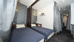 A hotel room with two beds, a small window, a bedside table with a lamp, and a shower area. - Hostel Hideaway (Tokyo)