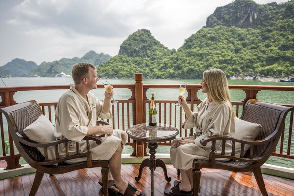 Two people seated at a table on a boat deck with a view of green hills and a body of water.