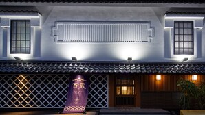 Ein traditionelles japanisches Gebäude mit einem Ziegeldach, einem hölzernen Eingangstor und einem violetten Banner mit goldener Schrift.