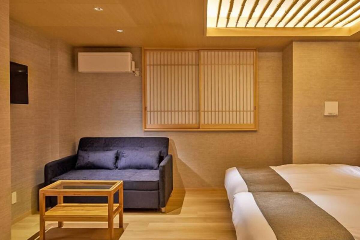 A modern hotel room with a sofa, a bed with pillows, a small wooden table, and a sliding shoji screen.