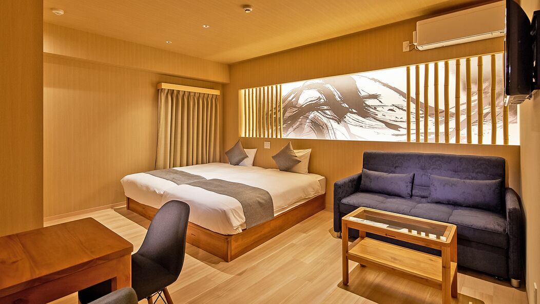A modern hotel room with a large bed, a sofa, a wooden coffee table, and a TV mounted on the wall.
