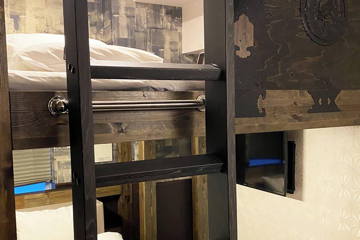 A bunk bed with a metal ladder, a wooden door, and a patterned wall.