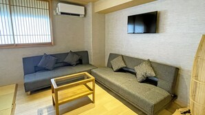 Ein modernes Wohnzimmer mit zwei Sofas, einem Holztisch, einem flachbildfernseher an der Wand und einer Klimaanlage.