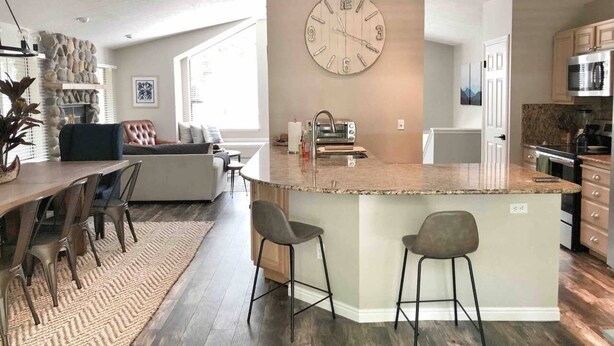 Une cuisine moderne dotée d’un îlot central, un coin repas avec une table et des chaises, et un espace de vie comprenant un canapé et une cheminée.