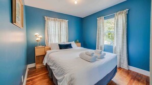 Un dormitorio con una cama grande, dos mesitas de noche y un ventanal con cortinas.