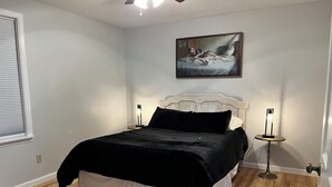 A bedroom with a bed, two bedside tables, a painting on the wall, and a window with blinds. - Waterfront Auke Bay cottage in Juneau (Juneau)