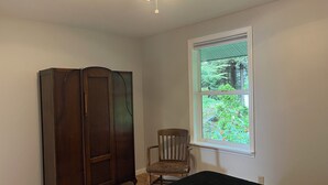 A room with a wooden wardrobe, a chair, a bed, and a window with a view of greenery. - Waterfront Auke Bay cottage in Juneau (Juneau)
