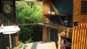Una terraza de madera con una silla amarilla, un lavamanos y una estantería con utensilios de cocina.