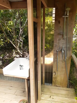 Une cabine de douche extérieure en bois, dotée d’un lavabo intégré.