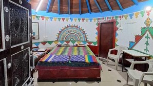 A room with a sloped ceiling, a bed with colorful bedding, a ceiling fan, and a decorative wall mural.