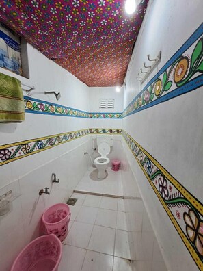 A narrow bathroom with a colorful floral ceiling, a toilet, a sink, and two pink buckets.