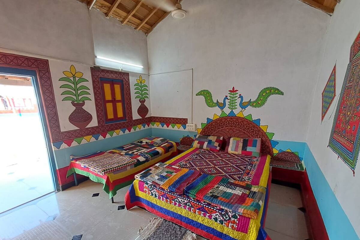 A room with two beds, colorful quilts, a window with a view, and decorative wall art.