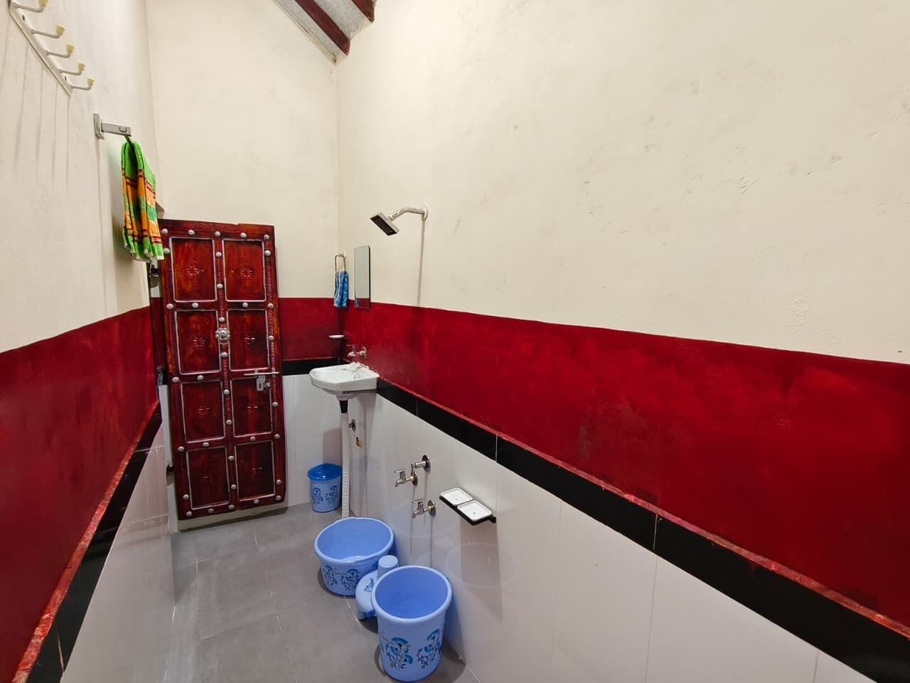 Un baño estrecho con pared de azulejos rojos y blancos, un lavabo blanco y dos cubos azules.
