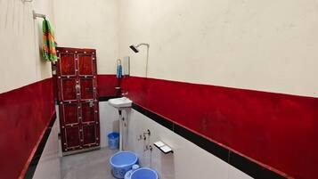 Un baño estrecho con pared de azulejos rojos y blancos, un lavabo blanco y dos cubos azules.