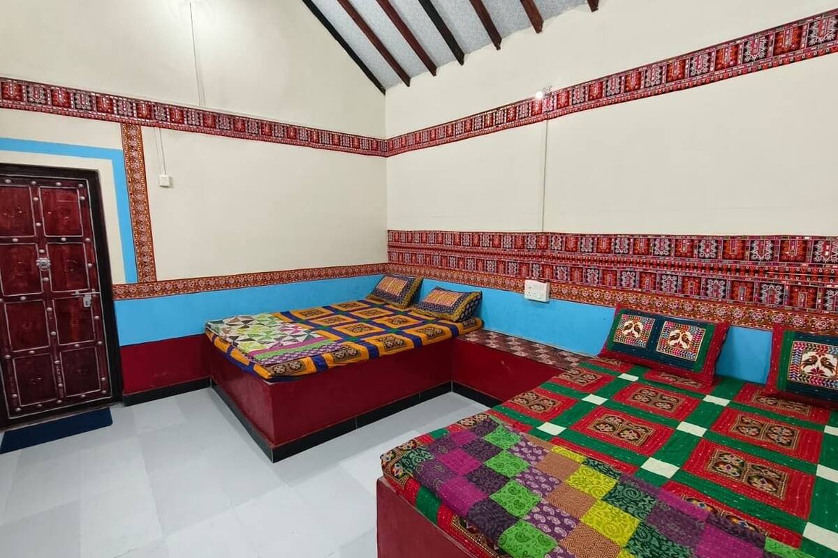 A room with a red and blue color scheme, featuring a large bed with a colorful quilt, a smaller bed, and a bench.