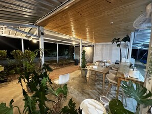An outdoor patio with wooden tables and chairs, surrounded by potted plants. - Mulberry Resort (Kra Buri)