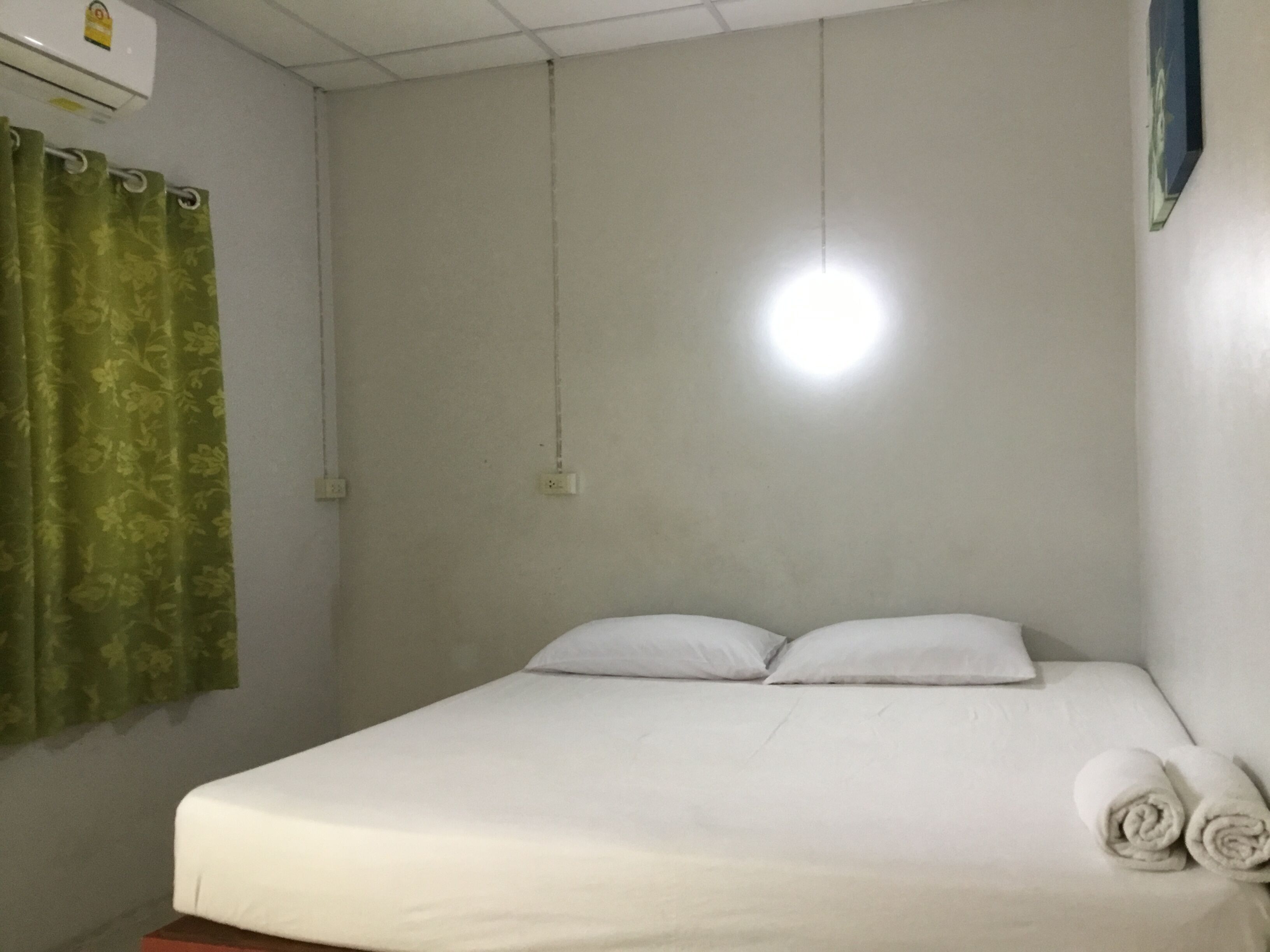 A single bed with white linens, a green curtain, and a wall-mounted light fixture.