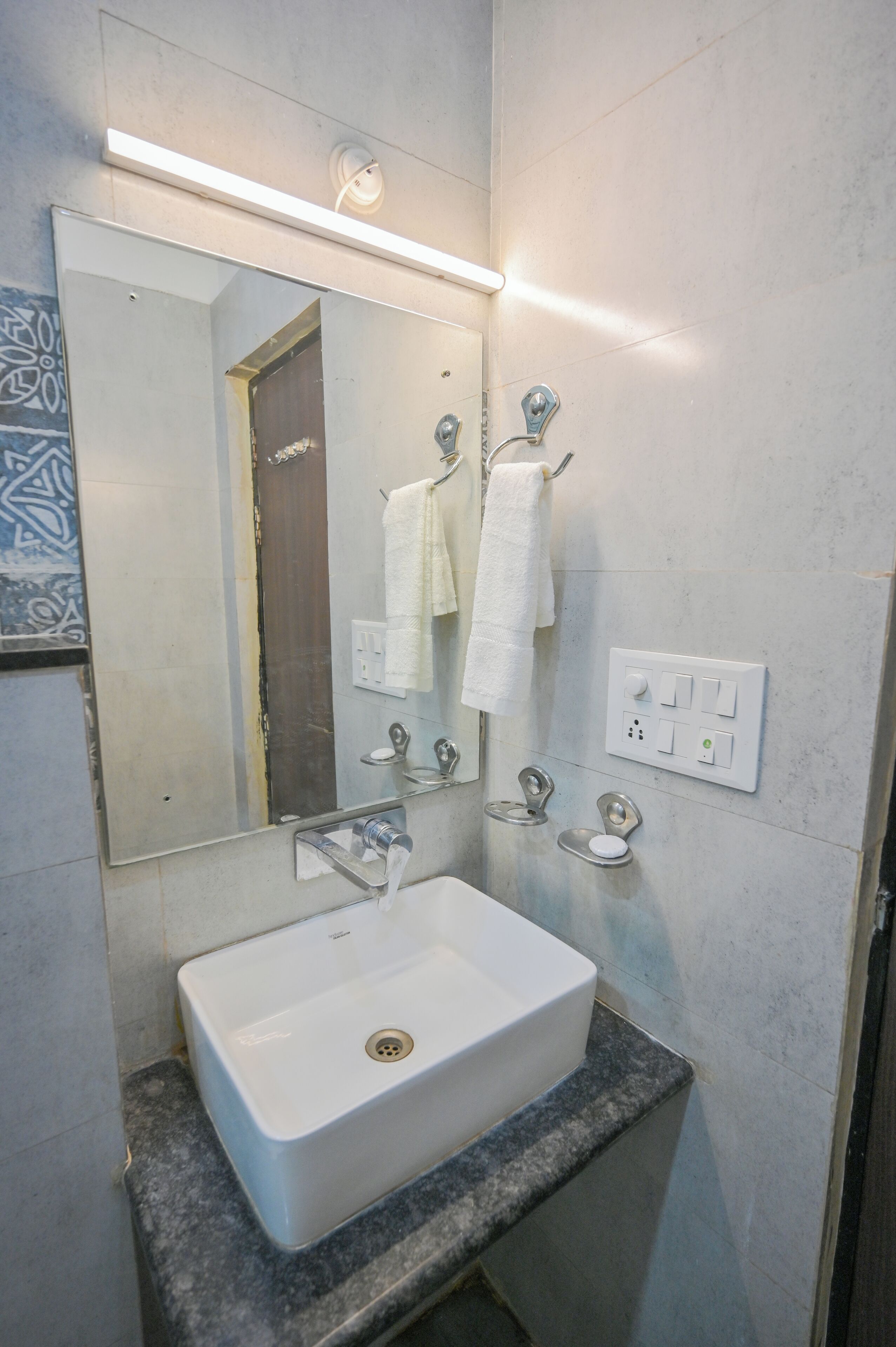 Un baño con lavamanos blanco, un espejo, toallero e iluminación.