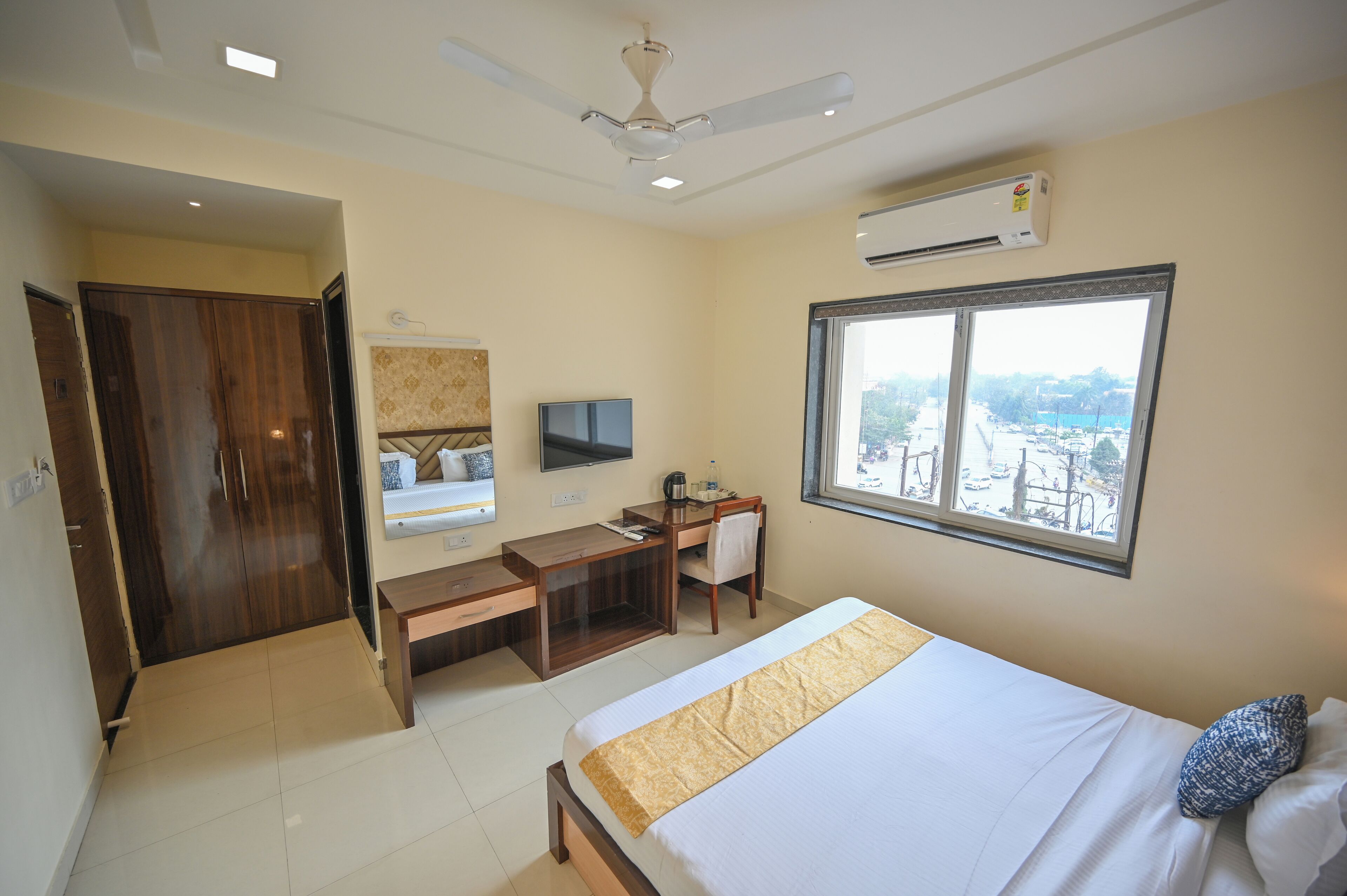 A hotel room with a bed, desk, chair, TV, and a large window with a view.
