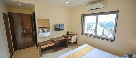 Habitación de hotel con cama, escritorio, silla, televisor y un ventanal con vistas.