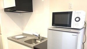 A compact kitchen with a built-in microwave on top of a refrigerator, a stainless steel sink, and a black range hood. - Mr.KINJO Miki24 in front of Makishi Station (Naha)