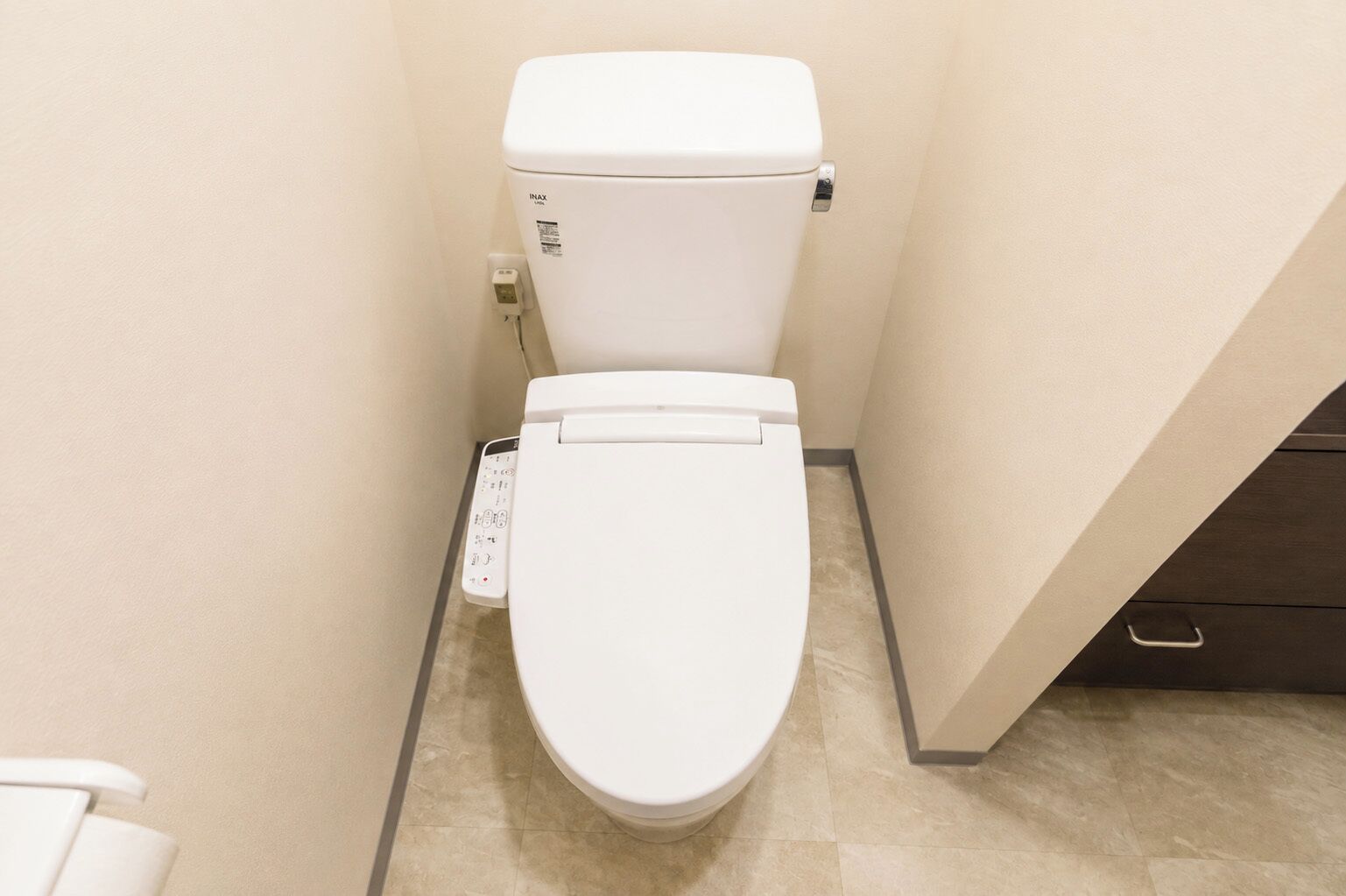 A toilet with a control panel, a wall-mounted flush handle, and a tiled floor.