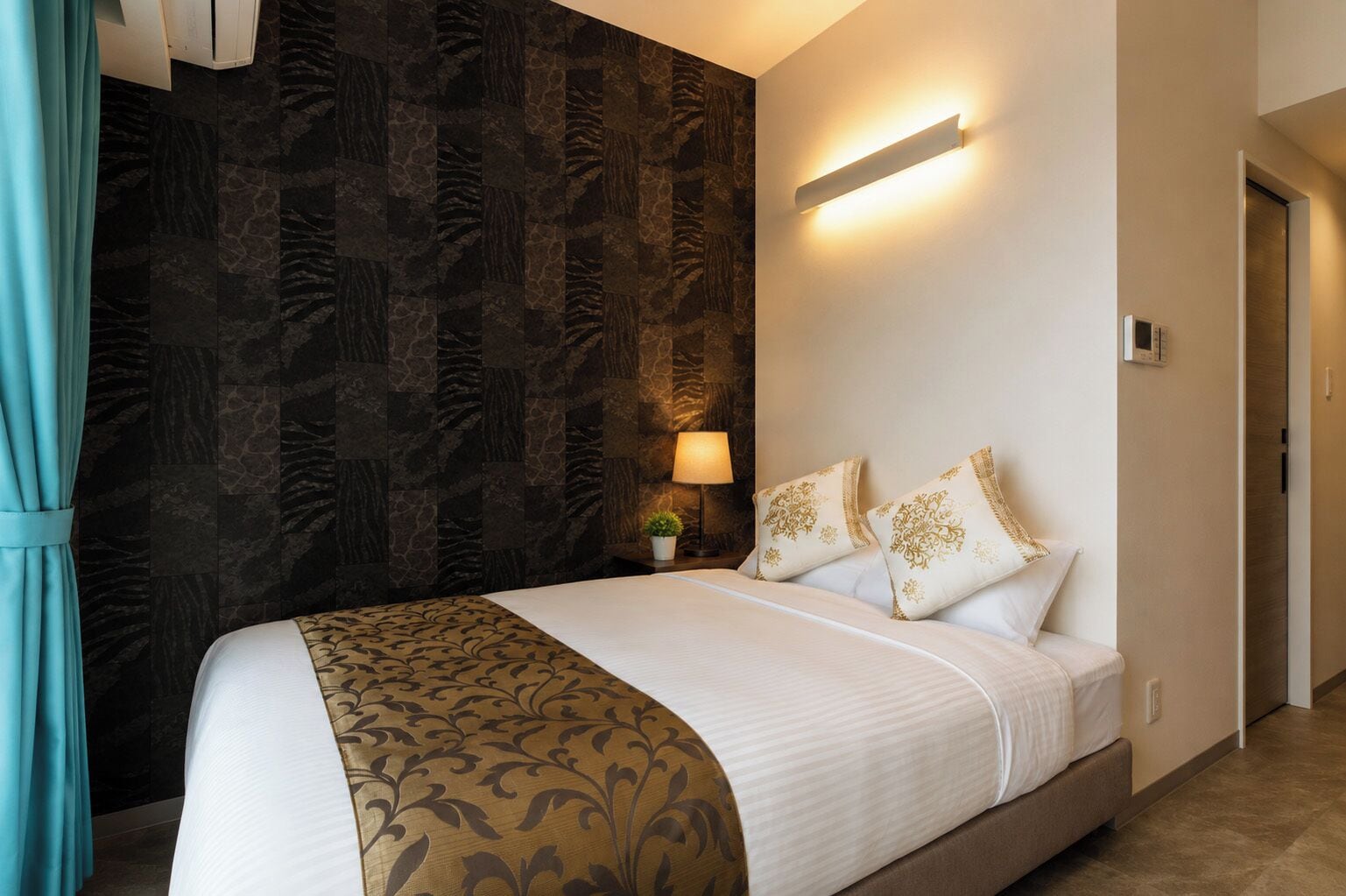 Una habitación de hotel con una cama grande, una mesita de noche con lámpara y una lámpara de pared.
