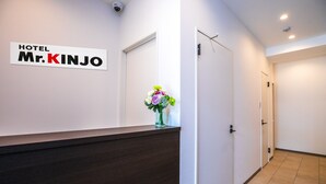 A hotel reception area with a dark reception desk, a wall sign reading "HOTEL Mr. KINJO", and a vase with flowers. - Mr.KINJO Miki24 in front of Makishi Station (Naha)