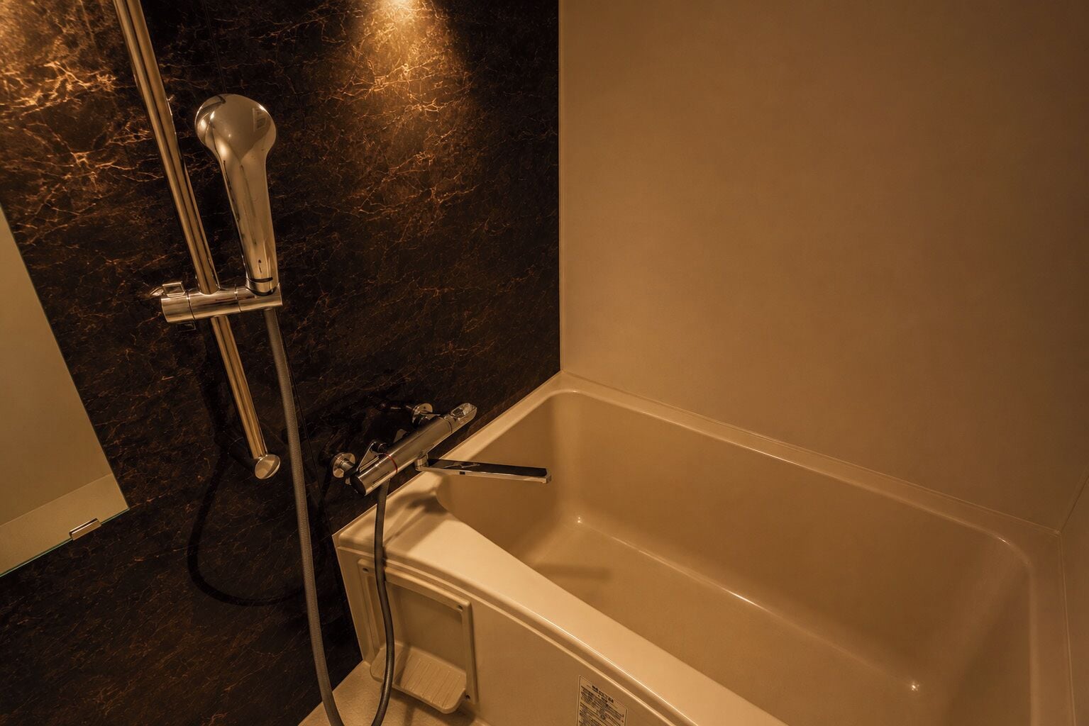 A bathroom with a bathtub, a showerhead, and a marble wall.