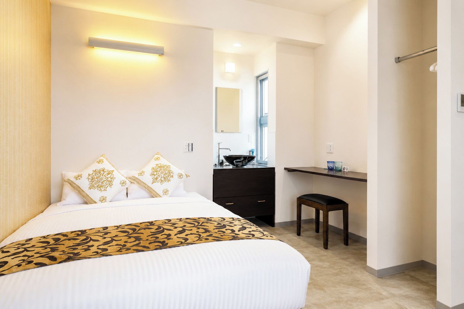 A hotel room with a bed, bedside table, and a small stool.
