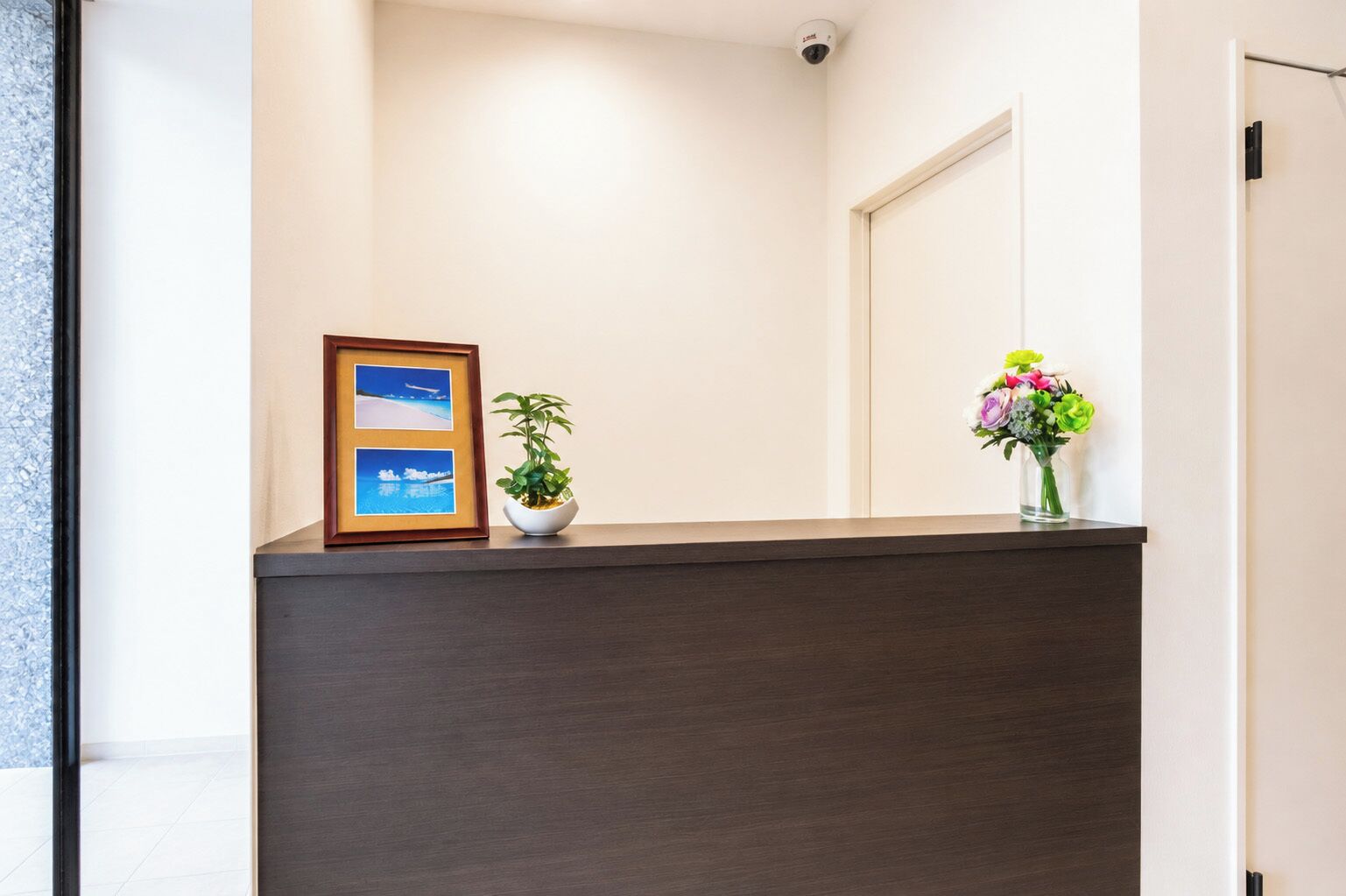 Un comptoir d’accueil orné d’une photo encadrée, d’une plante en pot et d’un vase de fleurs.