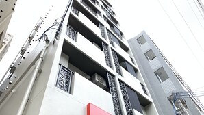 A multi-story building with a modern architectural design, featuring balconies with intricate railings and a prominent red sign with the brand name "Mikimoto" on the lower level. - Mr.KINJO Miki24 in front of Makishi Station (Naha)