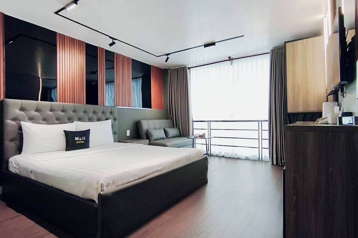 Une chambre d’hôtel moderne dotée d’un grand lit, d’un canapé, d’un bureau et d’un balcon avec des rideaux.