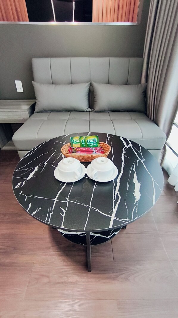 A modern living room with a grey sofa, a round black table with white marble-like patterns, and a wicker basket with packaged goods.