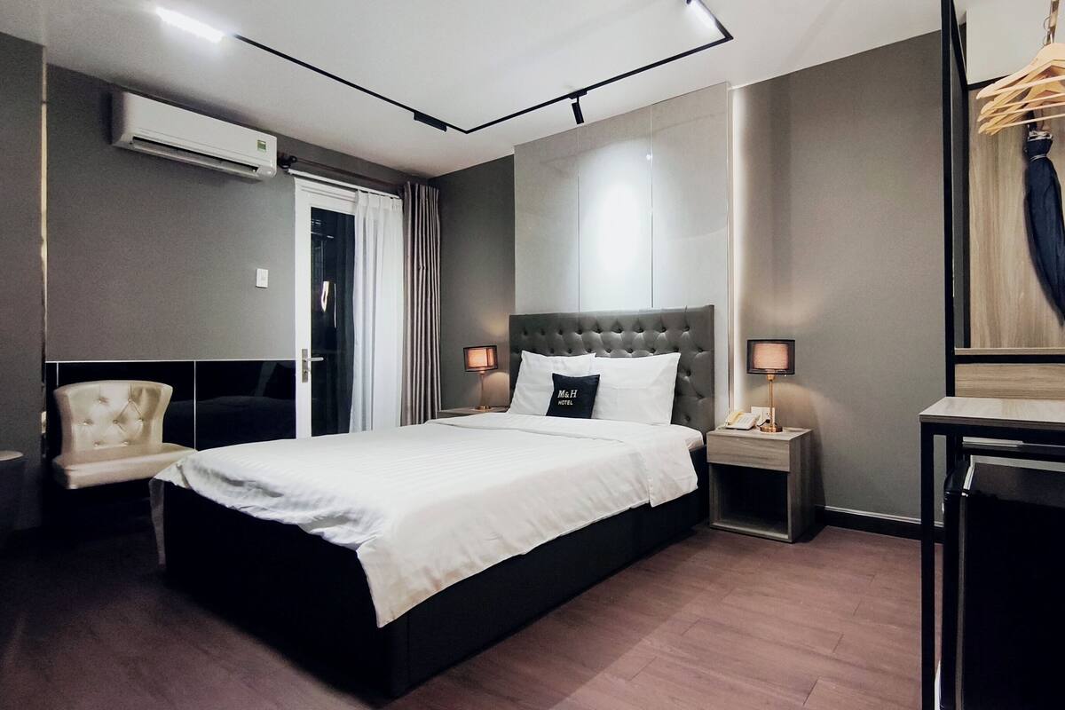 Une chambre d’hôtel comprenant un lit, des tables de chevet, un bureau, une chaise, un miroir et un appareil de climatisation.
