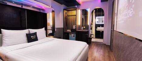 A hotel room with a bed, a nightstand, a desk, a mirror, and a bathroom visible through an open door.
