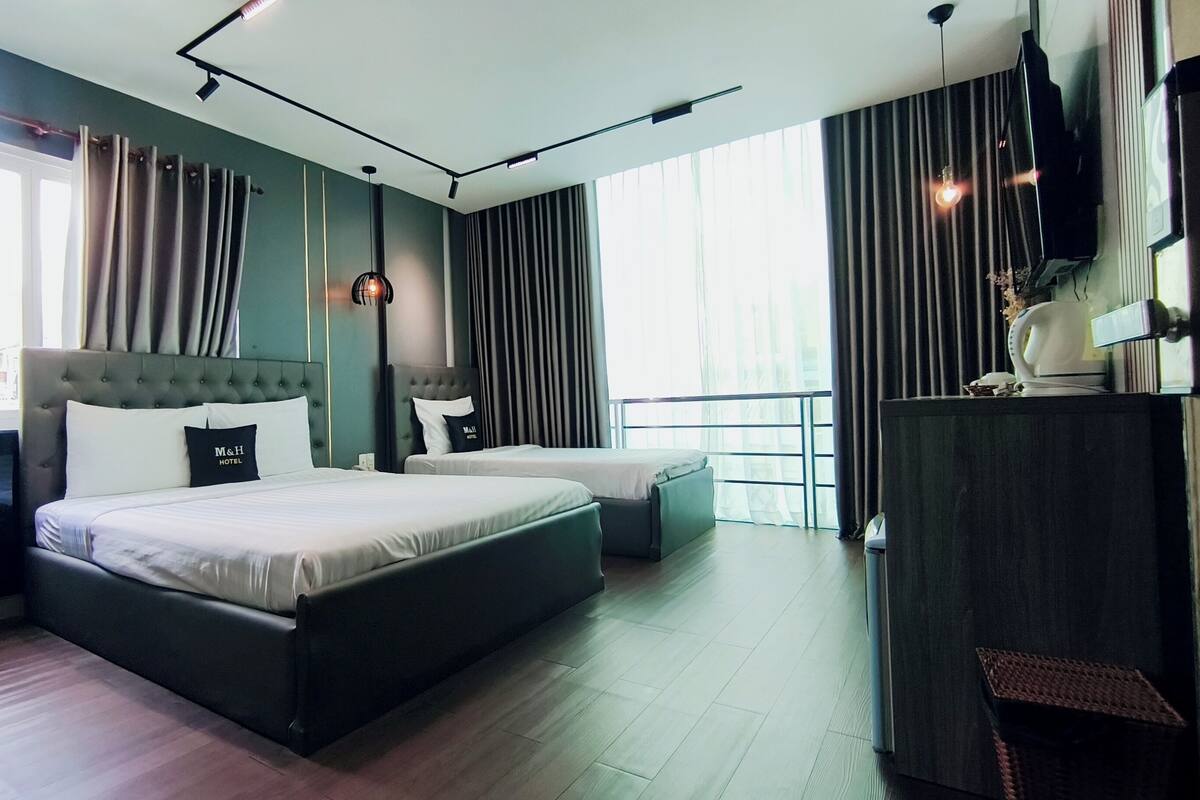 Une chambre d’hôtel moderne avec un grand lit, deux tables de chevet, un bureau et un balcon avec des rideaux.