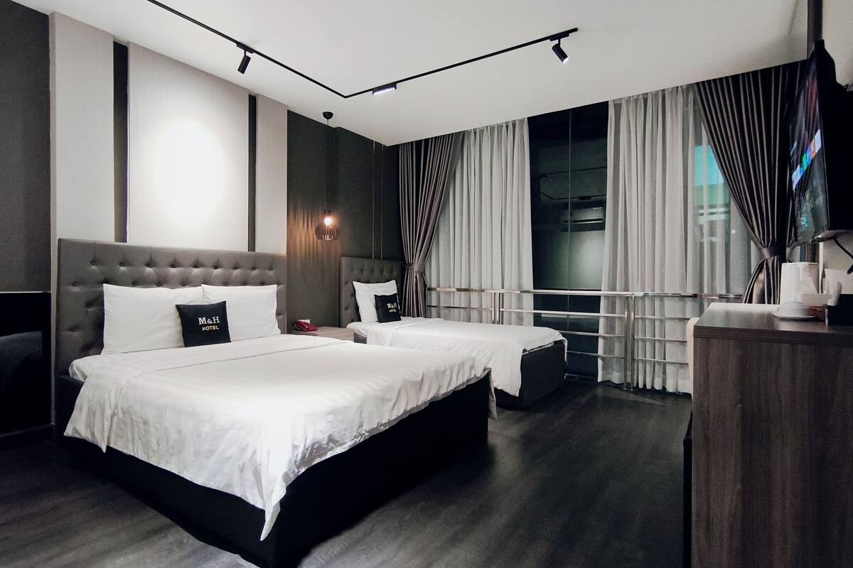 Une chambre d’hôtel avec un grand lit, deux tables de chevet, un bureau, une télévision et une fenêtre avec des rideaux.