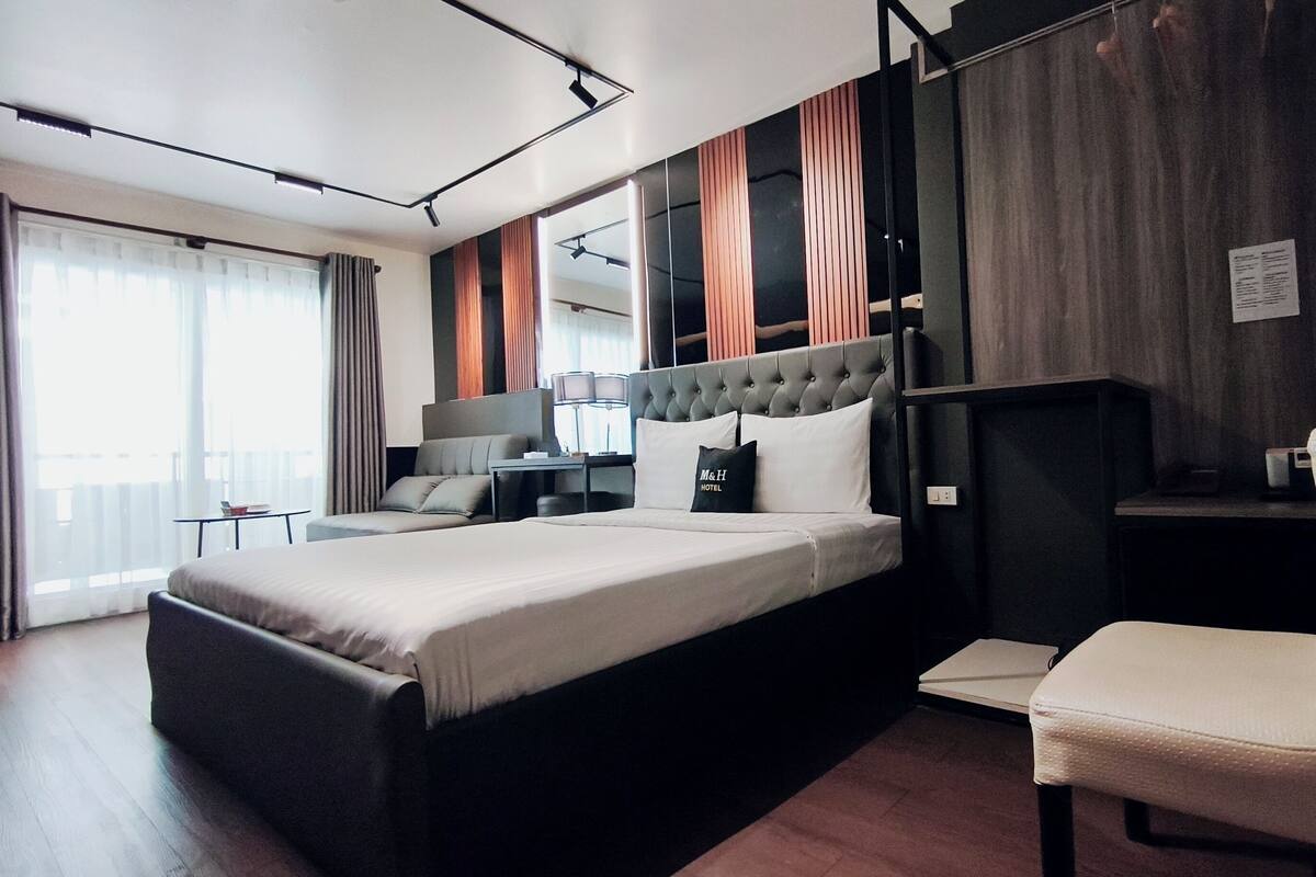 Une chambre d’hôtel moderne dotée d’un grand lit, d’un coin salon, d’un bureau et offrant une vue sur l’extérieur.