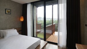 Une chambre d’hôtel avec un grand lit, un bureau en bois et un balcon donnant sur un paysage verdoyant.