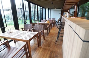 Un restaurante con mesas y sillas de madera, ventanas amplias y una zona de bar.