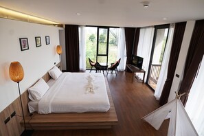 Una habitación de hotel moderna con una cama grande, un escritorio con televisor y un balcón con sillas.