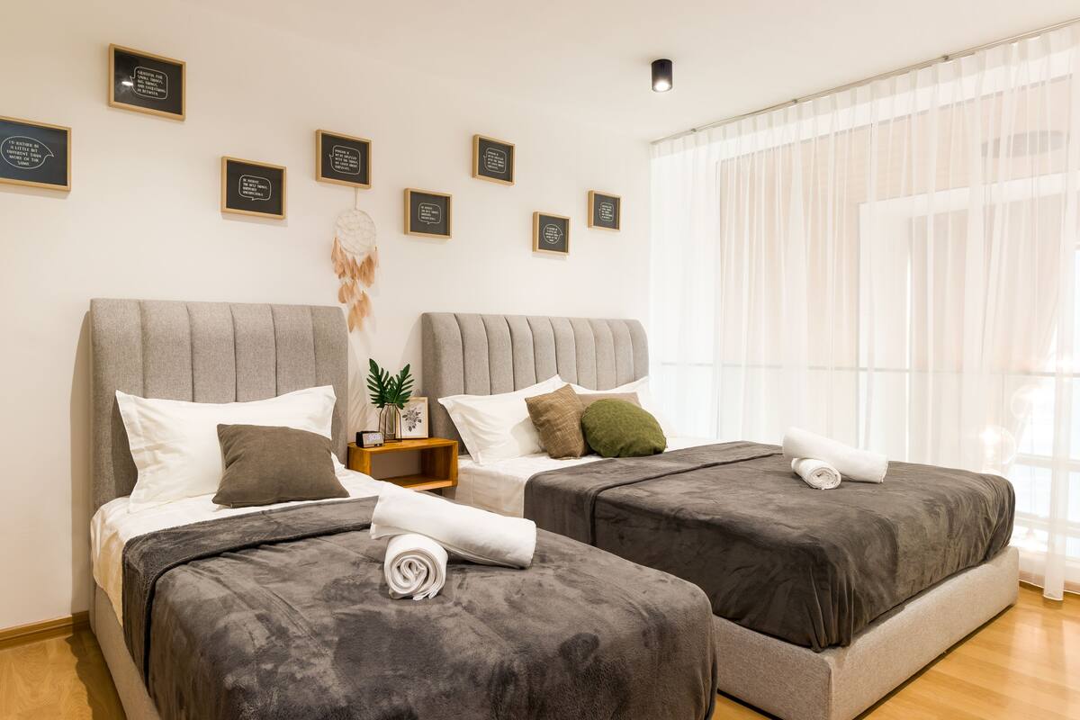 A hotel room with two beds, a small bedside table, a wall-mounted dreamcatcher, and framed inspirational quotes.
