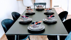 Mesa de jantar com cadeiras pretas, cada uma com um jogo americano trançado e um guardanapo vermelho amarrado com fita.