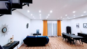 Uma sala de estar moderna com um sofá preto, uma mesa de jantar e uma televisão.