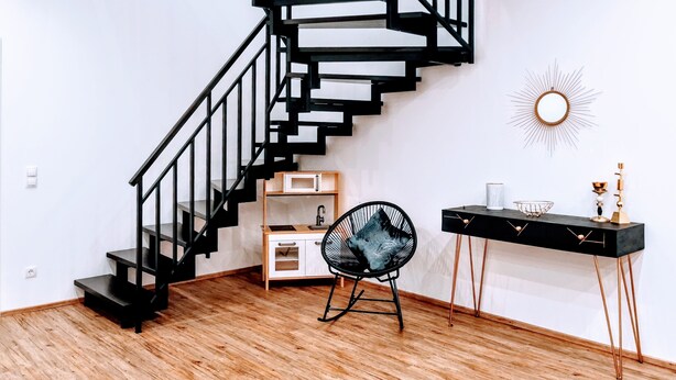 Interior moderno com escada espiral preta, piso de madeira, escrivaninha com cadeira e um elemento decorativo na parede.
