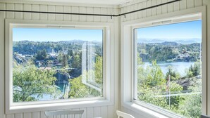 Una habitación con dos ventanas amplias que ofrecen vistas a un lago, árboles y montañas distantes.