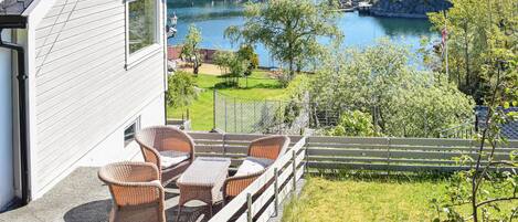 Une maison dotée d’un balcon donnant sur un lac, aménagée avec des fauteuils et une table en osier.