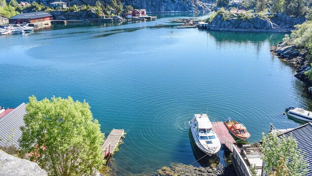 Un río tranquilo con barcos amarrados en un muelle, rodeado de riscos y vegetación.